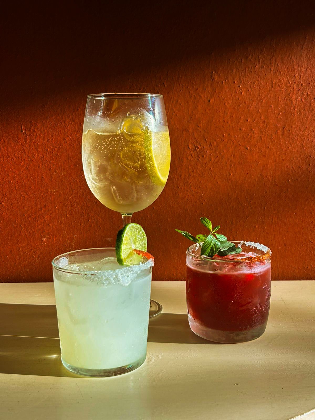 Tres cocteles de autor sobre barra de piedra con muro terracota