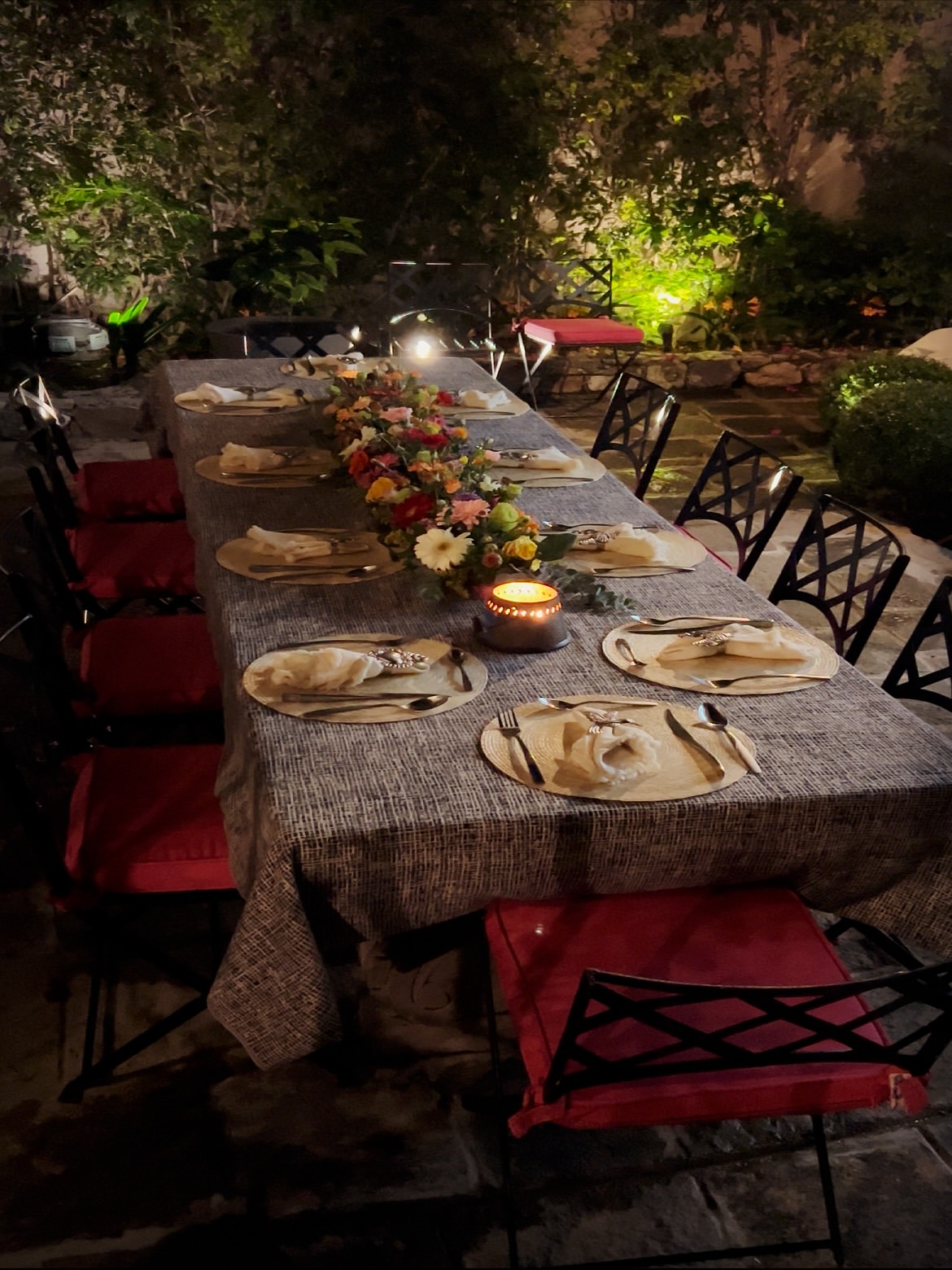Mesa de jardín montada de noche con flores, velas y vajilla dorada para una cena privada